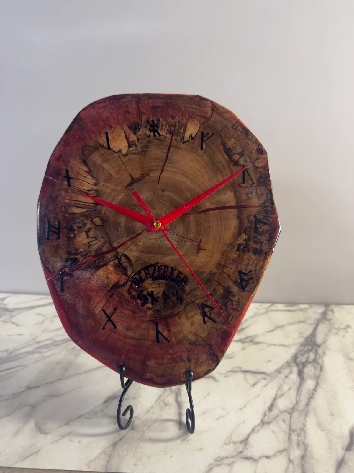 Wood clock with red hands and dark symbols arranged around the face.