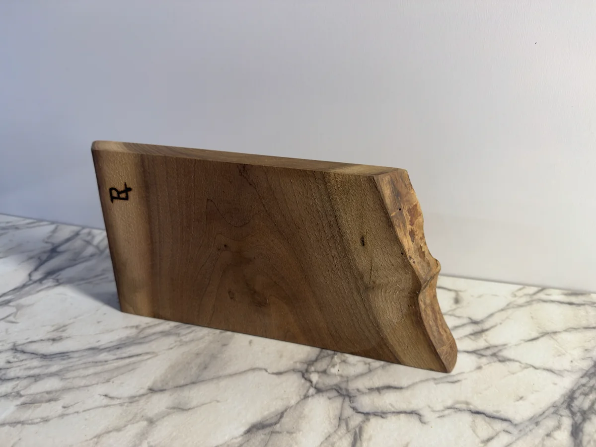 Side view of the cutting board showing its thick profile, irregular outer edge, and small dark maker mark.