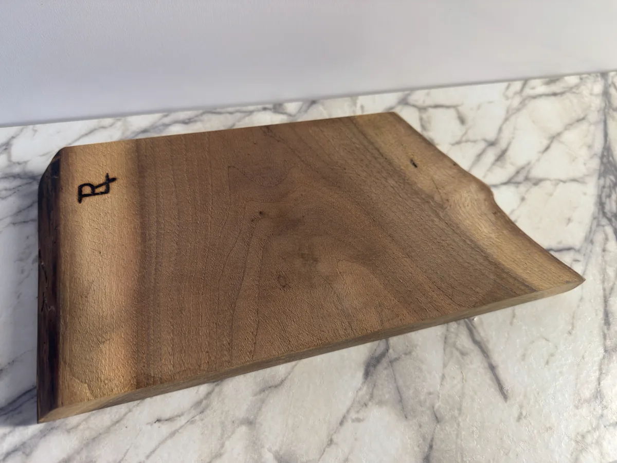 Rectangular wood cutting board with a dark maker mark near one corner.